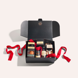 Open black gift box with red ribbon containing various items on a light gray background